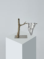 A single Dalí-style melting clock towel by DAMNART$ draped over a sculptural branch on a minimalist pedestal.
