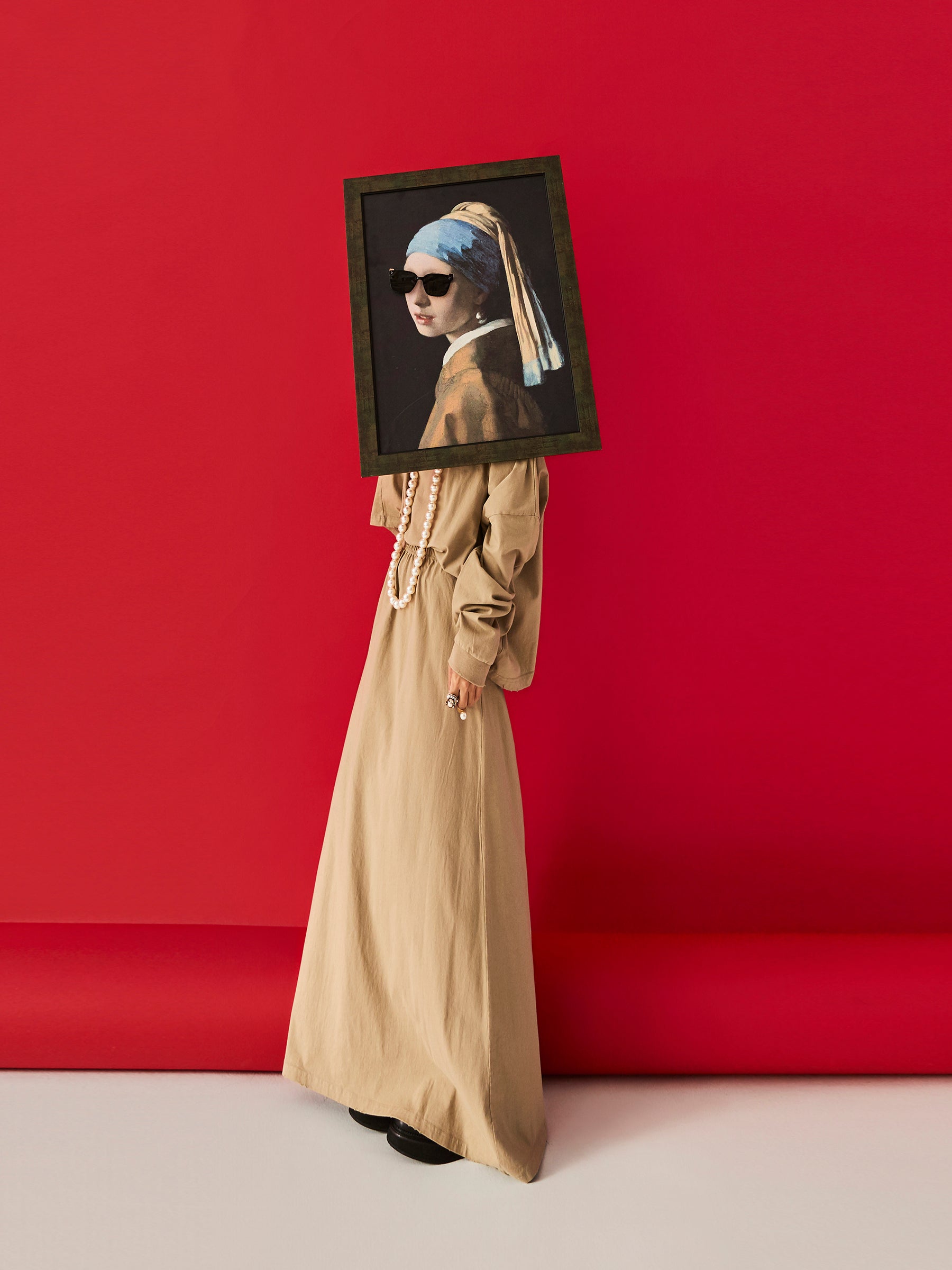 DAMNARTS Girl with a Pearl Earring glasses holder worn in a lifestyle scene with a bold red background, featuring black sunglasses and strong visual contrast.