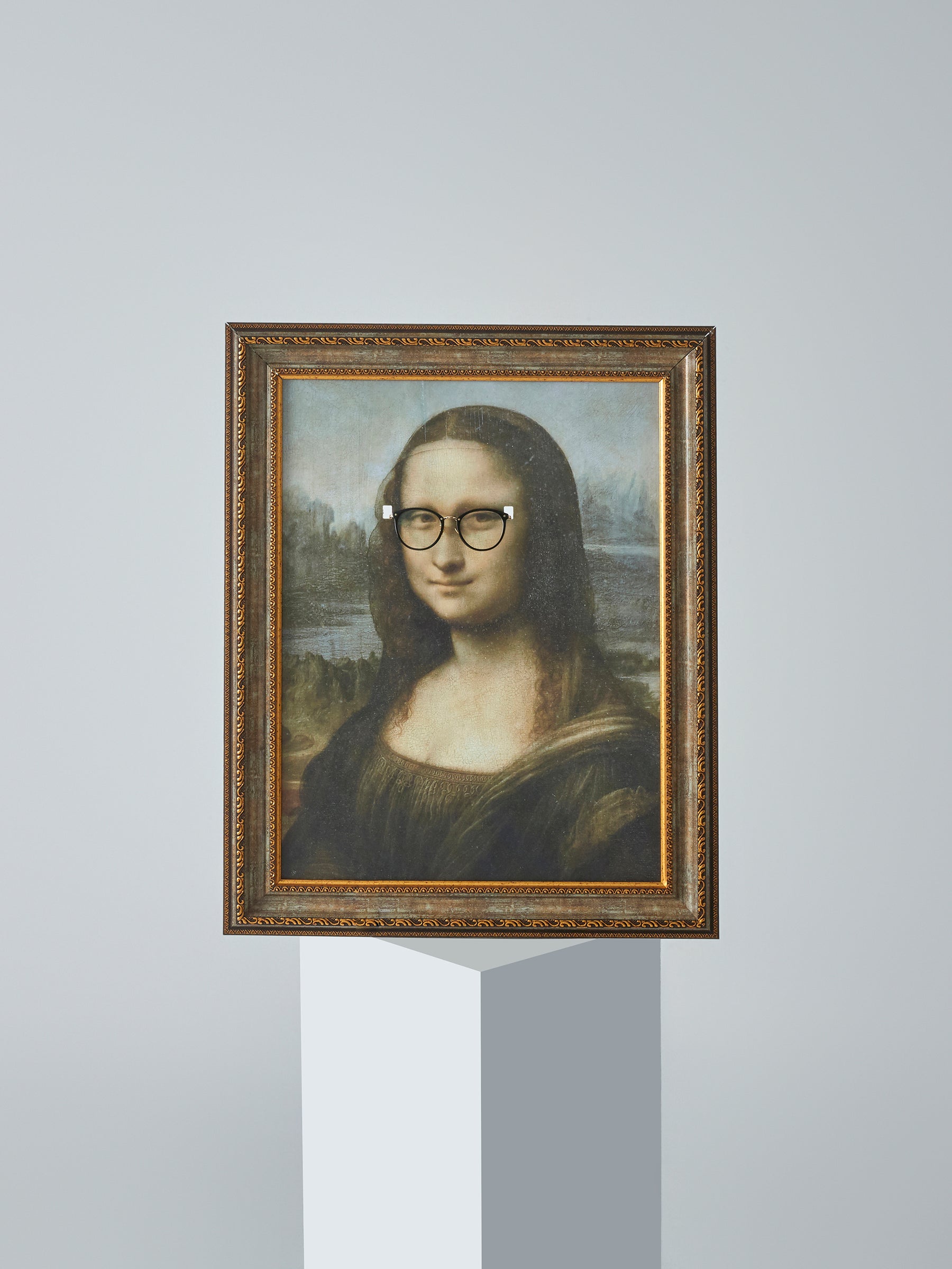 DAMNARTS Mona Lisa glasses holder displayed on a pedestal with round optical glasses, highlighting art and function.