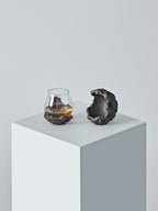 A DAMNARTS meteorite-style whisky glass set displayed on a minimalist white pedestal, featuring a textured meteorite base and a sculptural half-sphere holder.