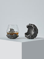 Close-up of the DAMNARTS meteorite whisky glass and matching sculptural holder, designed with rugged crater-like textures.