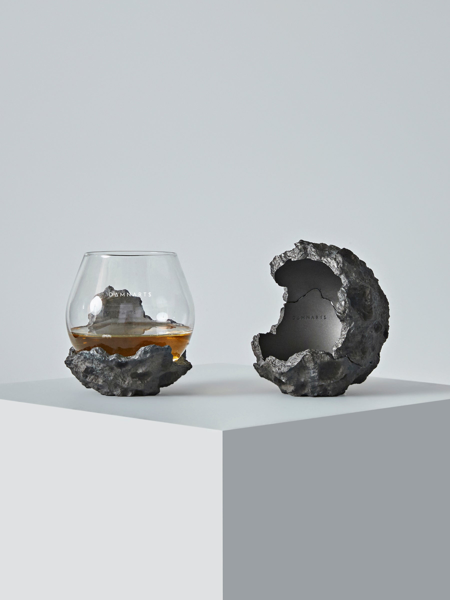 Close-up of the DAMNARTS meteorite whisky glass and matching sculptural holder, designed with rugged crater-like textures.