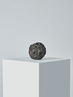 A standalone DAMNARTS meteorite-style whisky coaster shown on a minimalist pedestal, emphasizing its rough, cratered texture.