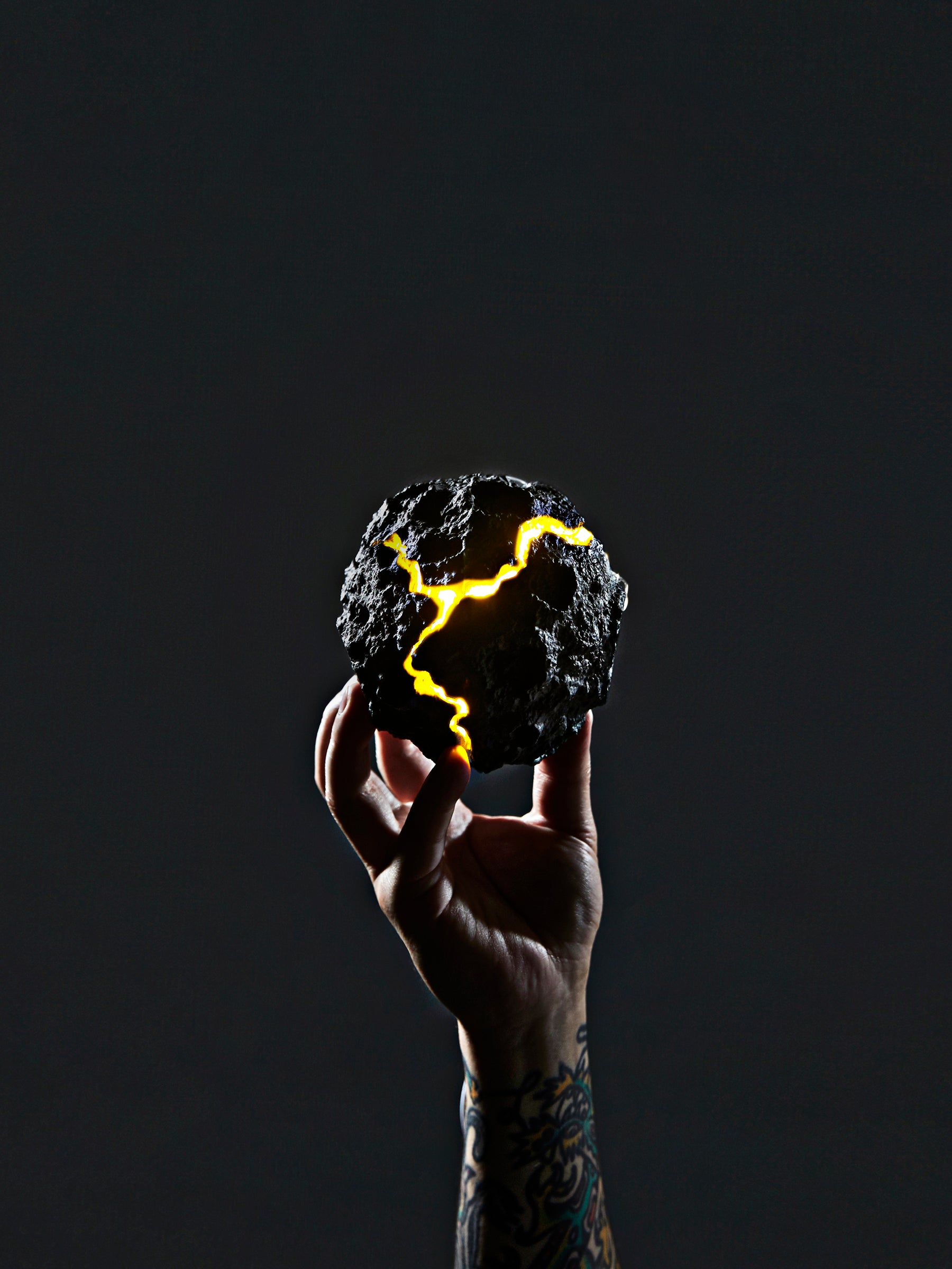 A hand holding a DAMNARTS meteorite-inspired sculptural piece glowing with golden cracks against a dark background.