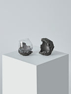 DAMNARTS meteorite whisky glass and cratered holder presented on a clean pedestal in a minimalist studio setting.